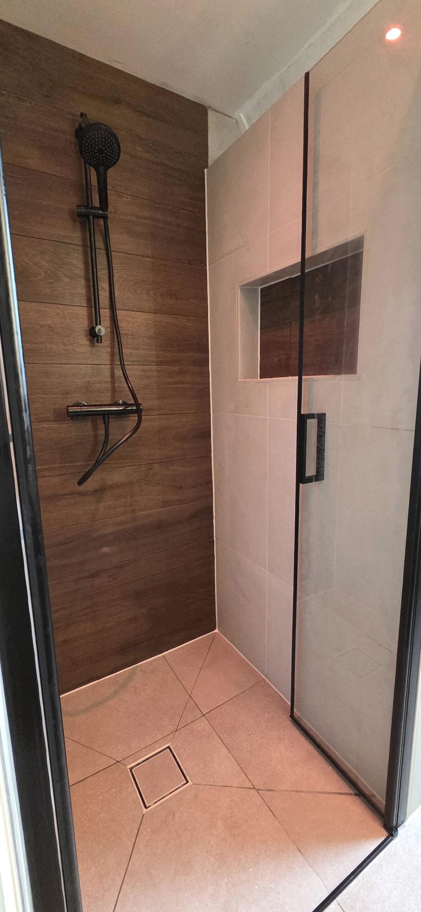 Geplaatste douche met houtlookwand, zwarte doucheset en glazen deur