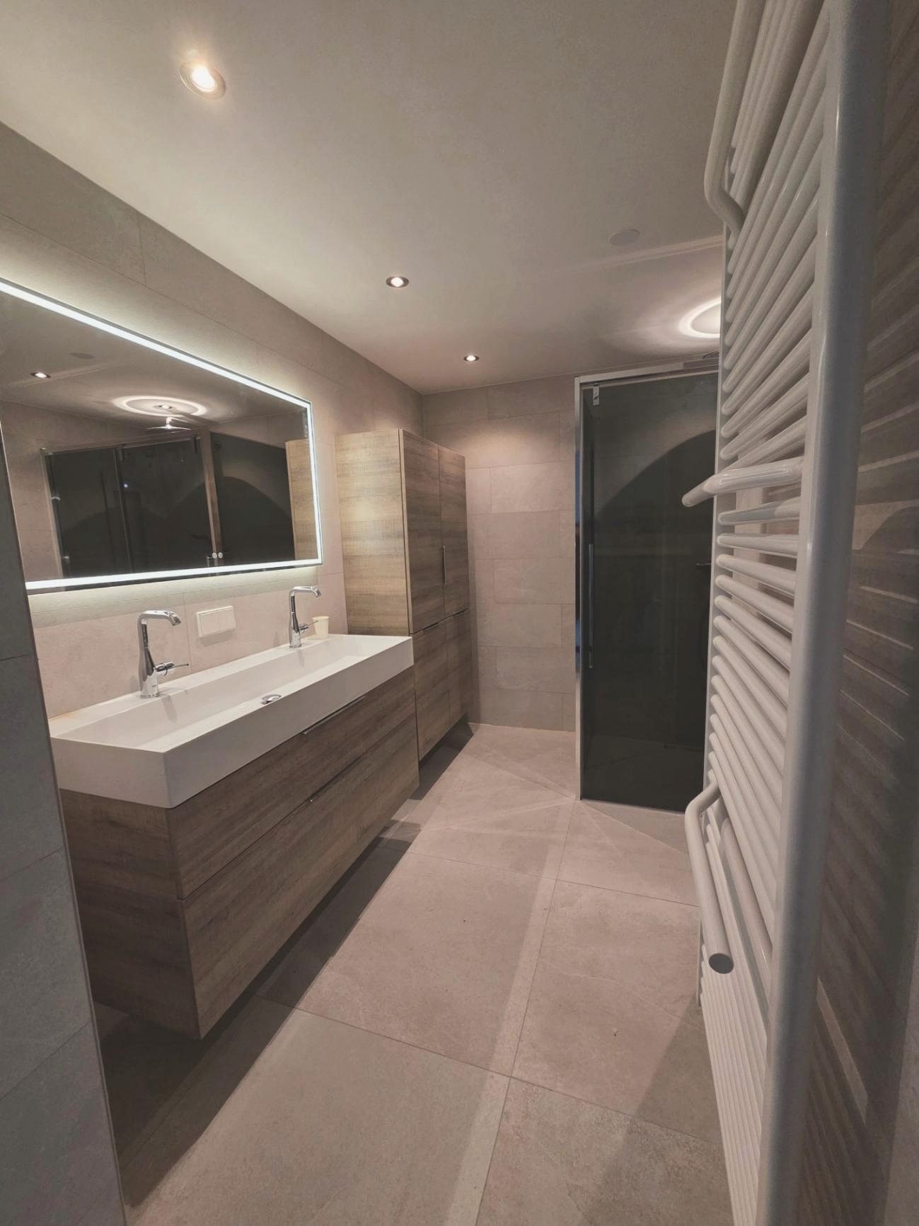 Geplaatste badkamer met een zwevend houten meubel, dubbele wastafel en verlichte spiegel