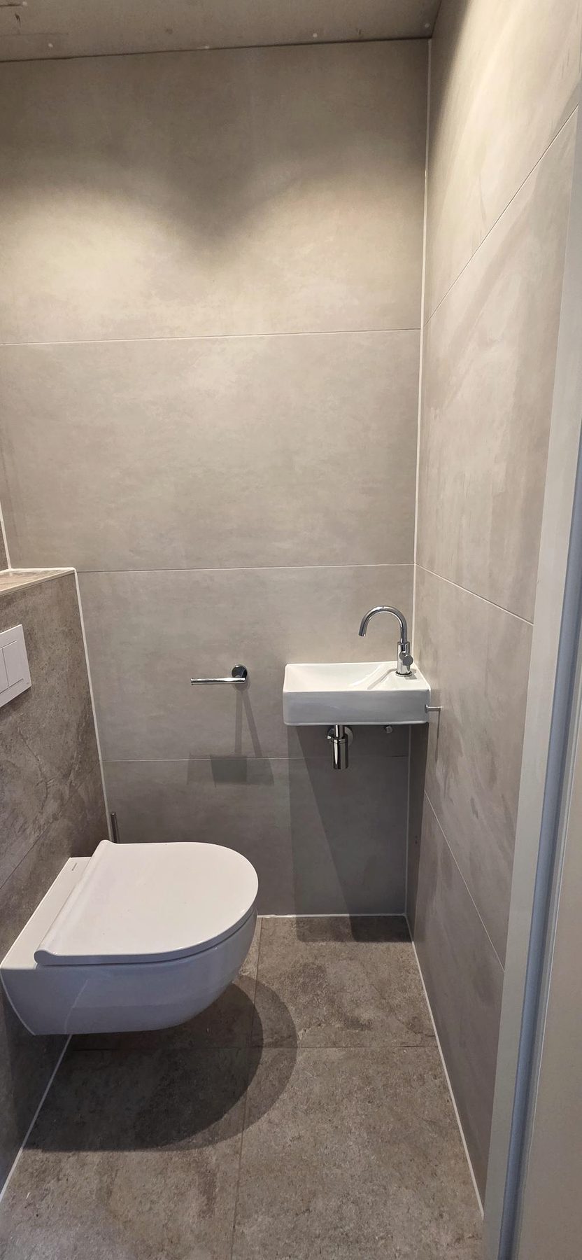 Geplaatst toilet in grijze tegels met een klein fonteintje