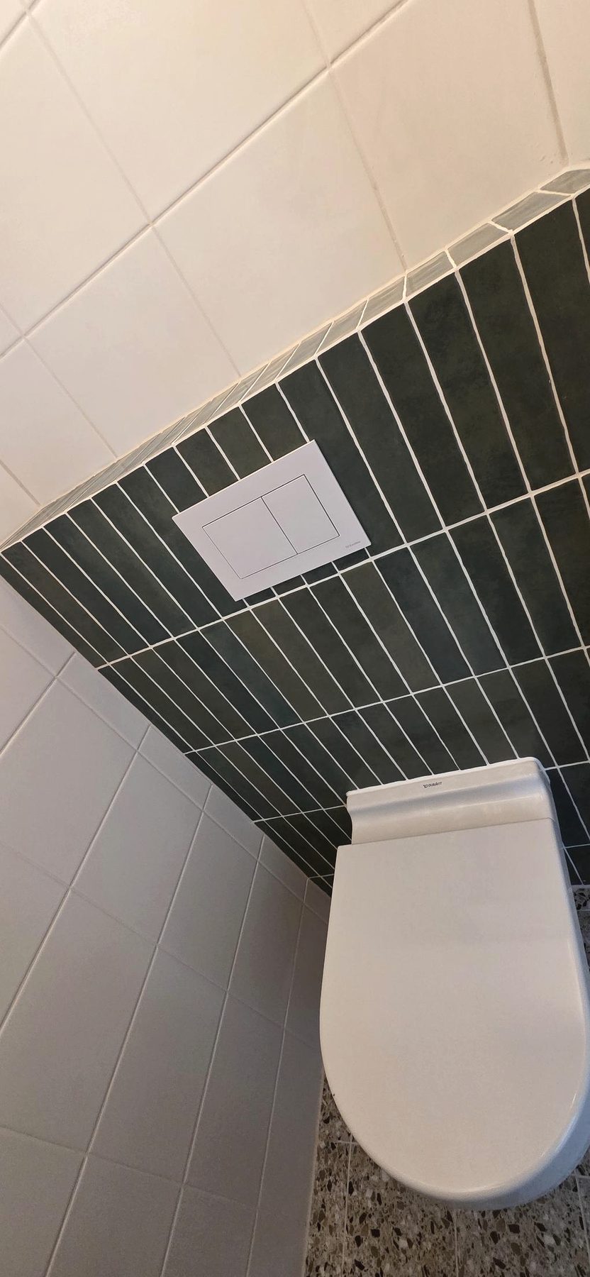 Geplaatst toilet met donkergroene wandtegels en terrazzo vloer
