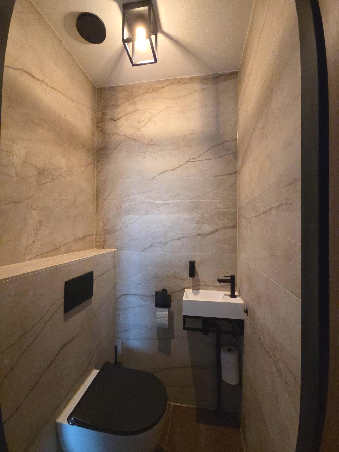 Geplaatst toilet in marmeren tegels met zwart fonteintje